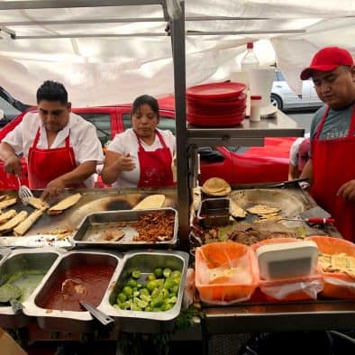 Food vendors preparing street food and wine pairings at a lively night market.