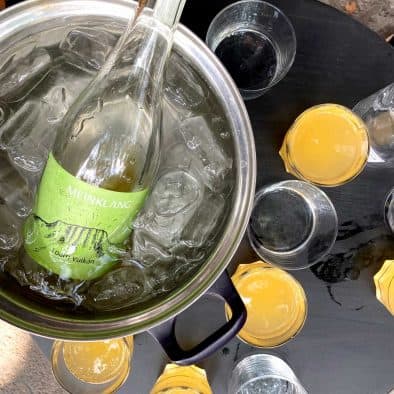 Bottle of wine chilling in ice with glasses of orange juice and water on a street table.
